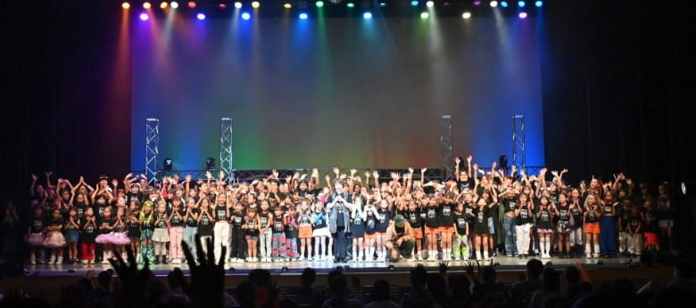 ステージ上で手をあげる多くのダンス生徒たち